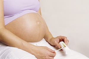 Glucose test during pregnancy: Pregnant woman checking the colour of a reagent strip used in a Clinistix urine test. The test detects <a  href='/glossary/g#glucose' data-toggle='popover' data-trigger='hover' title='glucose' data-content='1807' >glucose</a> sugar levels in urine. The brown colouration on the reagent strip indicates a positive (abnormal) result.