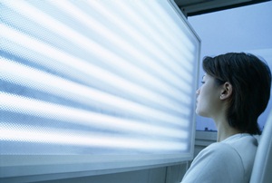 Woman undergoing phototherapy in front of a light screen. Phototherapy is used to treat jet lag.